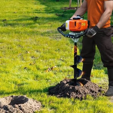 Gas-powered post hole auger drilling into ground